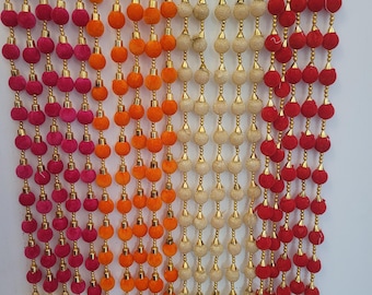 May include: A set of three decorative door hanging garlands with pom-poms in red, orange, and beige. Each garland has gold beads and tassels.