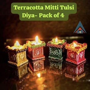 May include: Set of four terracotta diyas, each with a different coloured design and a lit candle inside. The diyas are decorated with traditional Indian symbols and are labelled "Terracotta Mitti Tulsi Diya - Pack of 4".