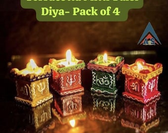 May include: Set of four terracotta diyas, each with a different colored design and a lit candle inside. The diyas are decorated with traditional Indian symbols and are labeled "Terracotta Mitti Tulsi Diya - Pack of 4".