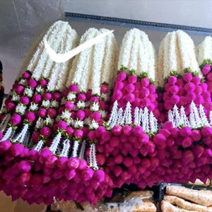 Puede incluir: Se exhiben varias guirnaldas de flores blancas y magenta. Las guirnaldas están compuestas por flores blancas y esponjosas en la parte superior, que dan paso a flores esféricas de color magenta. Acentos blancos, como encaje, separan las capas de flores.