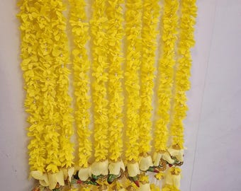 May include: Bright yellow floral garlands hanging vertically against a white wall. The garlands are made of small, petal-like flowers and are strung together with white string. The bottom of each garland features white and yellow floral accents with decorative embellishments.