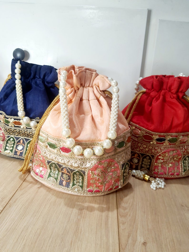 Puede incluir: Tres bolsas de cord&oacute;n con ribete de perlas y detalles bordados. Las bolsas son en tonos azul, melocot&oacute;n y rojo.