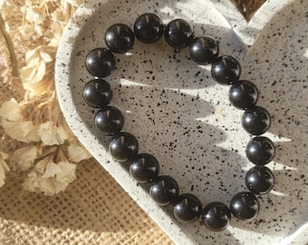 May include: A black beaded bracelet with shiny, round beads. The bracelet is on a white heart-shaped dish.