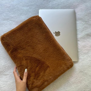 Puede incluir: Una funda para portátil de piel sintética marrón con cierre de cremallera. La funda se muestra con un portátil en su interior.