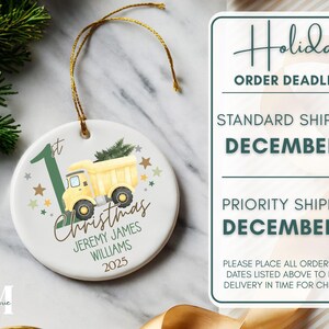 May include: A white ceramic Christmas ornament with a yellow dump truck carrying a Christmas tree. The ornament has the text "1st Christmas" and a name and year. A gold string is attached for hanging.