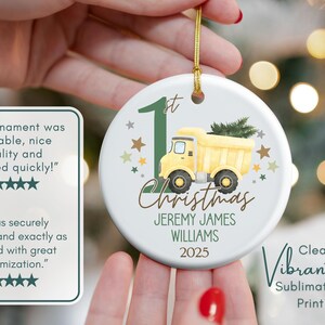 May include: Round Christmas ornament with a yellow dump truck, green accents, and the text "1st Christmas" and a name. The ornament has a gold string for hanging. The design is a clear, vibrant sublimation print.