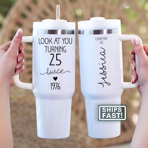 May include: Two white insulated tumblers with handles. One tumbler has the text "LOOK AT YOU TURNING 25 twice 1976" and the other has "CHAPTER 50 Jessica" in black script. Both tumblers have a white lid and a straw.