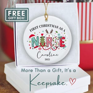 May include: A white ceramic Christmas ornament with the text "First Christmas as a Nurse" and the name "Caroline" and the year "2025". The ornament has a gold string for hanging and is in a white gift box. The text "More Than a Gift, It's a Keepsake" is below the box.