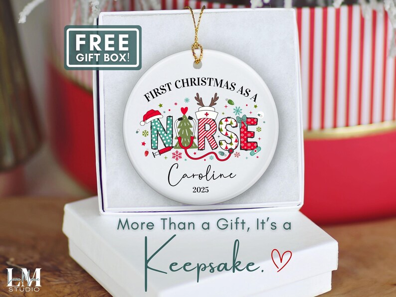 May include: A white ceramic Christmas ornament with the text "First Christmas as a Nurse" and the name "Caroline" and the year "2025". The ornament has a gold string for hanging and is in a white gift box. The text "More Than a Gift, It's a Keepsake" is below the box.