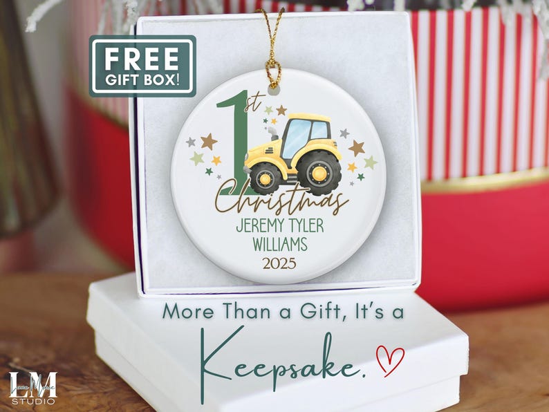 May include: A white ceramic Christmas ornament featuring a yellow tractor with a blue cab, the text "1st Christmas", and personalized details. The ornament is in a white gift box with the text "More Than a Gift, It's a Keepsake."