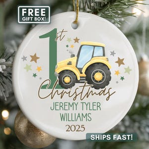 May include: A white ceramic Christmas ornament featuring a yellow tractor with black tires. The ornament includes the text "1st Christmas", personalized names, and the year 2025. Decorated with green and brown stars.