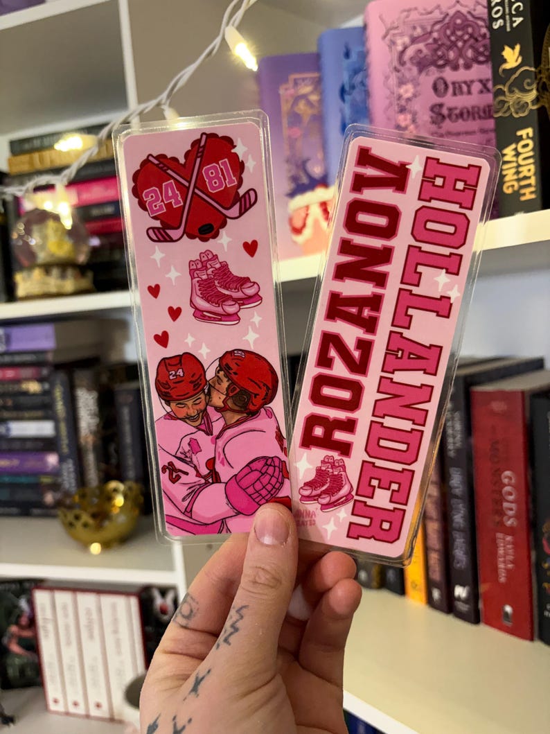 May include: Two pink hockey-themed bookmarks. One features a heart with crossed hockey sticks and the numbers 24 and 81. The other bookmark has the text "Rozanov Hollander" in pink. Both have illustrations of hockey skates and players.
