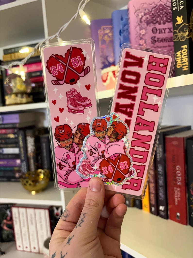May include: Two pink hockey-themed bookmarks. One features crossed hockey sticks, the numbers 24 and 81, and ice skates. The other bookmark reads "HOLLANDER" in pink block letters. Both have a clear plastic overlay.
