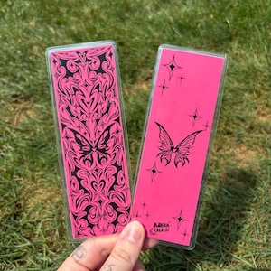 May include: Two pink bookmarks with black butterfly and star designs. One bookmark features a detailed butterfly and abstract pattern, the other has a butterfly and star accents. The text "KANNA CREATED" is visible on one bookmark.