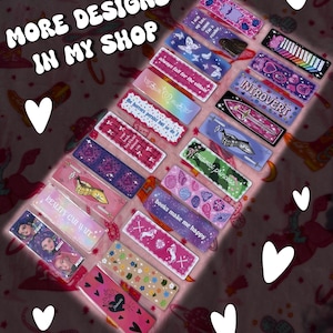 May include: A collection of rectangular bookmarks with various designs and text, including phrases like "always fall for the villain" and "books make me happy." The bookmarks feature colorful patterns, illustrations, and the text "MORE DESIGNS IN MY SHOP."
