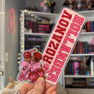 May include: A pink sticker with the words "ROZANOV HOLLANDER" in red, and a smaller sticker featuring two hockey players in pink uniforms kissing. The smaller sticker has the numbers 24 and 81 on it.