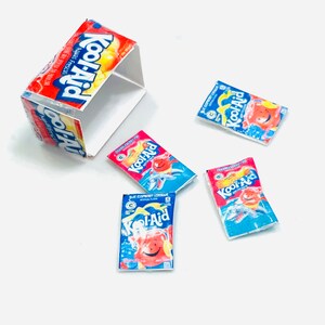 May include: Four individual packets of Kool-Aid drink mix. Two packets are red and blue with the text "Kool-Aid" and "Sharkleberry Lemonade". One packet is red and white with the text "Kool-Aid" and "Strawberry Lemonade". One packet is red and white with the text "Kool-Aid" and "Aguas Frescas".