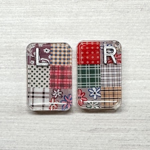 May include: Two rectangular charms featuring a patchwork design of various patterns including floral prints, plaid, and polka dots. The left charm displays a silver letter L, and the right charm displays a silver letter R, both with a glossy finish.
