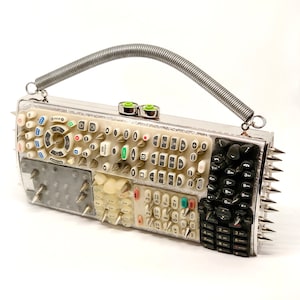 May include: A silver clutch purse with a spring handle and a design of multiple remote control buttons. The purse is covered in silver spikes.