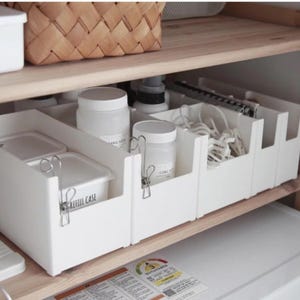 May include: White plastic storage bins with dividers, used to organise a shelf in a kitchen or bathroom. The bins are labelled with the text "REFILL CASE" and "CITRIC ACID".