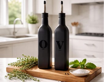 May include: Two matte black glass bottles with silver pour spouts. The left bottle features the letter O and the right bottle features the letter V, both in a bold black font. The bottles are tall, slender, and have a square base design.