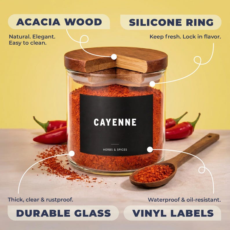May include: A clear glass spice jar filled with red cayenne pepper, featuring an acacia wood lid with a silicone ring. The jar has a black vinyl label with the text CAYENNE HERBS & SPICES. A wooden spoon rests nearby with loose pepper.