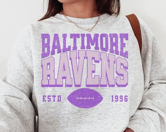 May include: A gray sweatshirt with a purple graphic that says "Baltimore Ravens" with a football graphic and the text "ESTD 1996".