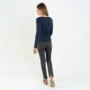 May include: A navy blue long-sleeved shirt with a scoop neck. The shirt is fitted and has a slightly cropped length. The model is wearing dark wash jeans and brown sandals.