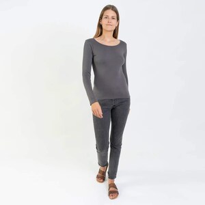 May include: A woman wearing a charcoal gray long-sleeved shirt with a scoop neck and dark gray jeans. She is wearing brown sandals.
