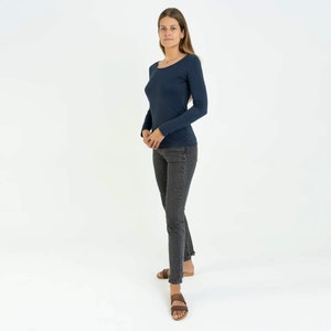 May include: A woman wearing a dark blue long-sleeved shirt and dark gray jeans. She is wearing brown sandals and has long brown hair.
