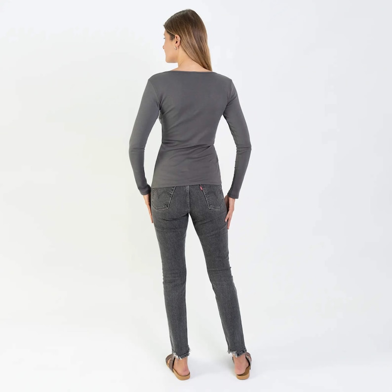 May include: A charcoal gray long-sleeved shirt with a scoop neck and a fitted silhouette. The shirt is worn with dark gray jeans.