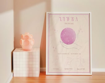 Pode incluir: Um pôster emoldurado branco com uma ilustração rosa e branca do signo do zodíaco Libra. O pôster tem o texto "Libra A Balança" e "22 de setembro - 22 de outubro". O pôster também tem três ícones que representam social, romântico e equilibrado.