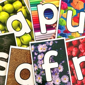 May include: A set of alphabet flashcards with different backgrounds. The letters are white with black outlines. The backgrounds include green apples, colourful pencils, umbrellas, a spider web, gold glitter, flowers, and raspberries.