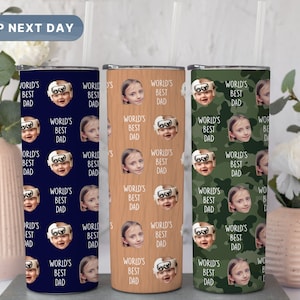 May include: Three stainless steel tumblers with lids and straws. Each tumbler features a different pattern: blue with white text and a repeated image of a child's face, brown with white text and a repeated image of a child's face, and green camouflage with white text and a repeated image of a child's face. The text on each tumbler reads "World's Best Dad".