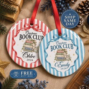 May include: Two round ceramic ornaments with red and blue striped backgrounds. Each features a stack of books, a teacup, and the text "Custome BOOK CLUB" with names "Chloe" and "Emily" and the year "2026" printed below, suspended by red ribbons.