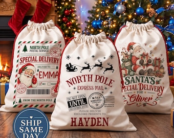 May include: Three off-white canvas drawstring gift bags with red cords. The left bag features a North Pole Postal Service label for Emma. The center bag reads North Pole Express Mail for Hayden. The right bag shows Santa for Oliver.