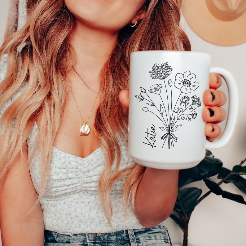 May include: White ceramic mug with a black line drawing of a bouquet of flowers and the name "Katie" on the front.