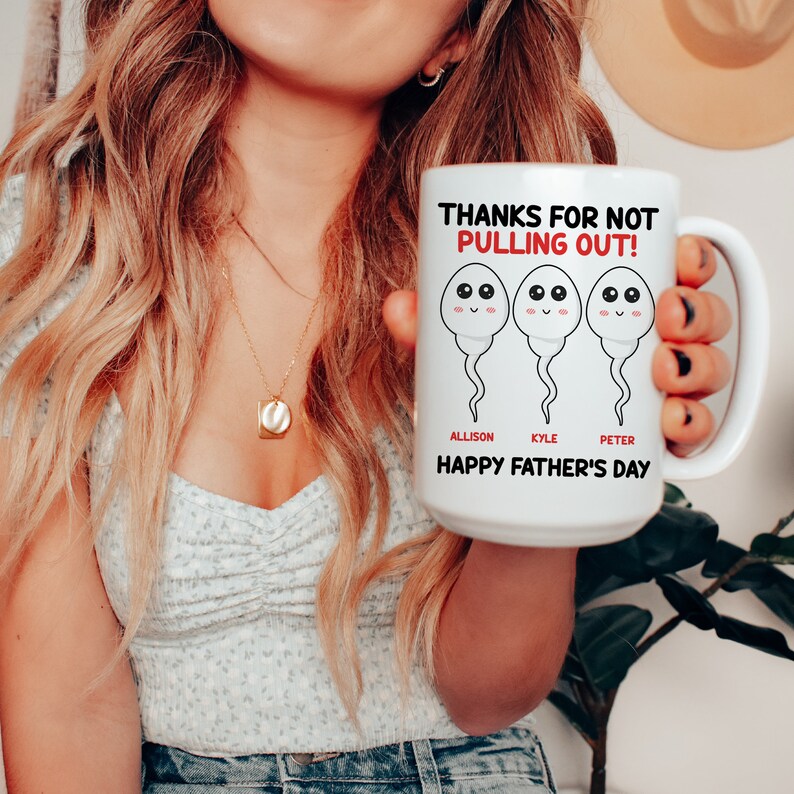 Op de afbeelding: Witte keramische mok met een humoristisch ontwerp voor Vaderdag. De mok heeft drie cartoon zaadcellen met lachende gezichten en de tekst "THANKS FOR NOT PULLING OUT!" samen met de namen Allison, Kyle en Peter, en "HAPPY FATHER'S DAY".