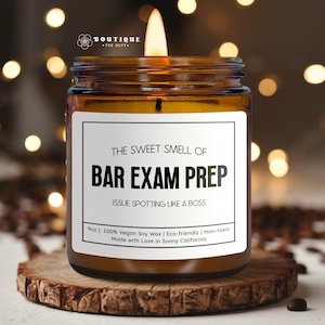 May include: A lit amber glass candle with a white label that reads "THE SWEET SMELL OF BAR EXAM PREP". The candle is on a wooden coaster. The candle is 9oz and made with vegan soy wax.