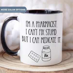 May include: White coffee mug with a black rim and handle. The mug has a black and white illustration of a pill bottle and a blister pack of pills. The text on the mug reads "I'm a pharmacist. I can't fix stupid. But I can medicate it."