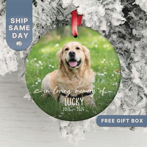 May include: A round, white, glass ornament with a photo of a golden retriever dog in a grassy field. The ornament has the text "in loving memory of LUCKY 2010 - 2024" written on it.