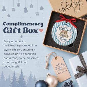 May include: A round ceramic ornament with blue and white vertical stripes, featuring a stack of books, a teacup, and the text "Custom Book Club" and "Emily 2026". It is topped with a red ribbon and presented in a square cardboard gift box.