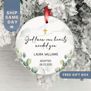 May include: Round ceramic ornament with a marble-like background, a gold cross, and the text "God knew our hearts needed you." Includes the name "LAURA WILLIAMS" and the date "06.23.2025". Decorated with watercolor-style leaves.