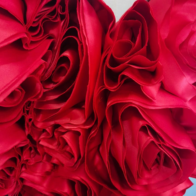 K&ouml;nnte beinhalten: Nahaufnahme eines leuchtend roten Stoffes mit einem geschichteten, ger&uuml;schten Design. Der Stoff scheint Satin oder ein &auml;hnliches Material zu sein, mit einem gl&auml;nzenden Glanz. Die Falten erzeugen ein rosen&auml;hnliches Muster mit einem weichen, strukturierten Aussehen.