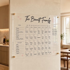 May include: A clear acrylic wall calendar featuring the text The Bennett Family, a monthly grid with daily schedule slots, a menu section, a grocery list, and a notes column. The board is mounted with four gold-toned metal standoffs at the corners.