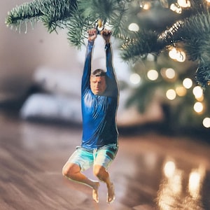 Pode incluir: Um enfeite de Natal azul e branco com uma pessoa pendurada em um galho. O enfeite é feito de um material durável e é perfeito para adicionar um toque único à sua decoração de Natal.