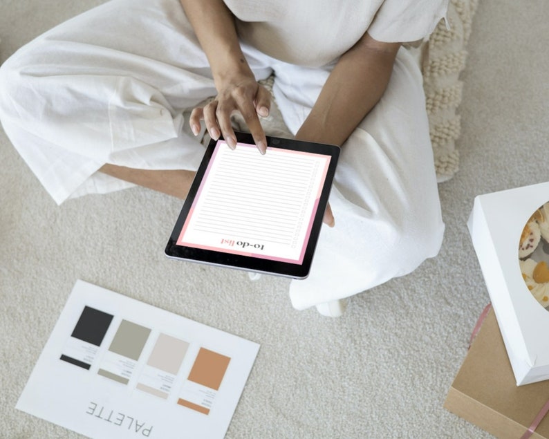 K&ouml;nnte beinhalten: Eine Person sitzt auf einem Teppich und verwendet ein Tablet, um eine To-Do-Liste zu erstellen. Der Tablet-Bildschirm zeigt eine rosa-wei&szlig;e To-Do-Listen-Vorlage. Neben der Person ist eine Farbpalette auf dem Boden sichtbar.