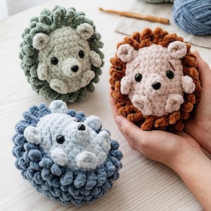 May include: Three handmade crochet lion toys in green, brown, and blue. The lions have round bodies and detailed manes. The image also shows balls of yarn and crochet hooks, suggesting a craft project.