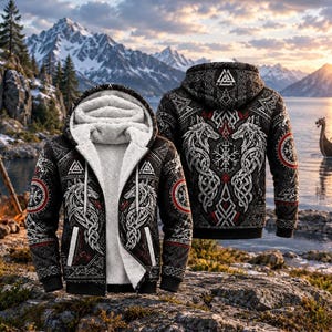 Op de afbeelding: Een zwarte hoodie met rits en witte sherpa-voering, voorzien van ingewikkelde wit-rode Noors geïnspireerde patronen, wolfillustraties en een Valknut-symbool op de rug en borst. Het ontwerp bevat een cirkelvormig Vegvisir-kompasmotief.