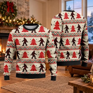 May include: A long-sleeve crew neck sweater in cream featuring a repeating pattern of dark brown Bigfoot silhouettes and red Christmas trees. The design includes horizontal bands of green and red zigzag stripes and black ribbed trim.